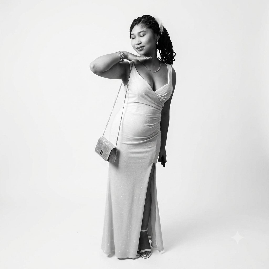 Black and white portrait of a woman in a flowing white gown holding a small shoulder bag, posed against a neutral background
